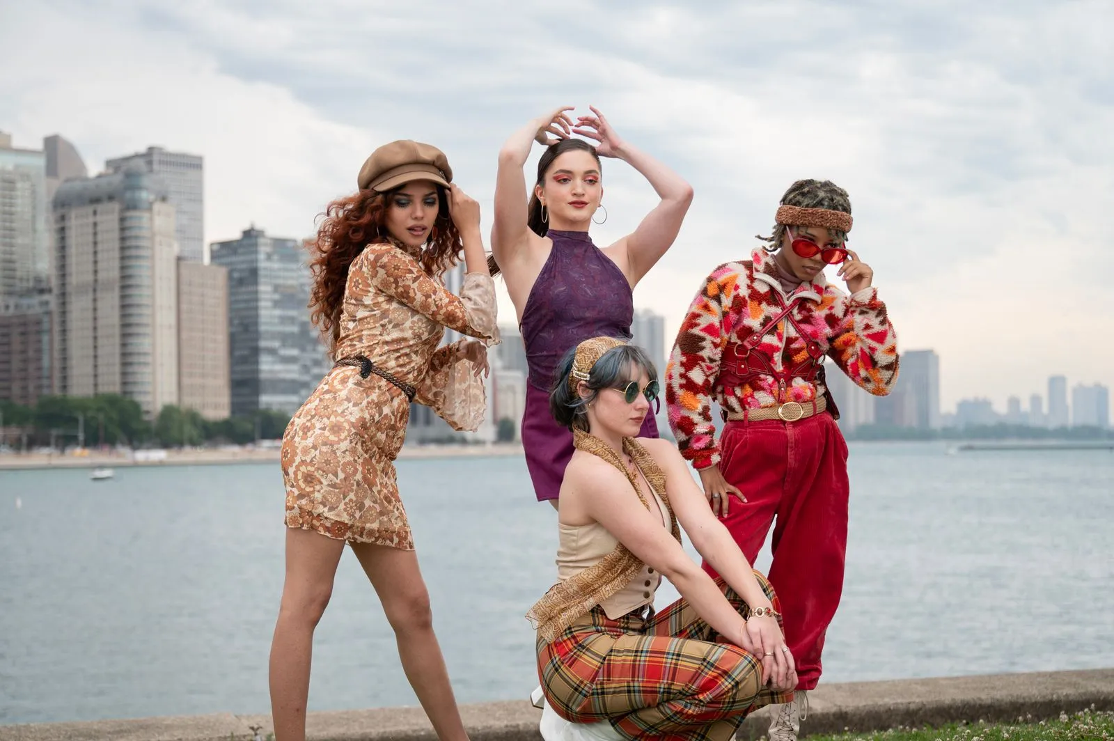 Stylishly dressed group of four posing in front of urban waterfront skyline, highlighting modern fashion trends.